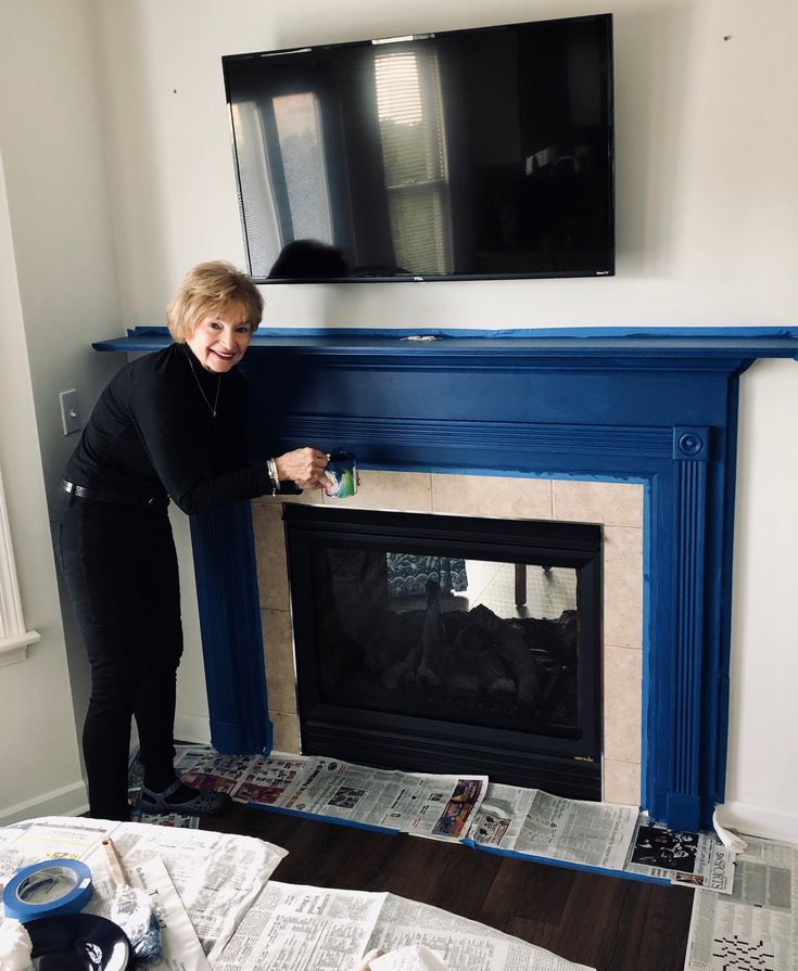 a woman standing in front of a blue fireplace with newspapers on the floor next to it