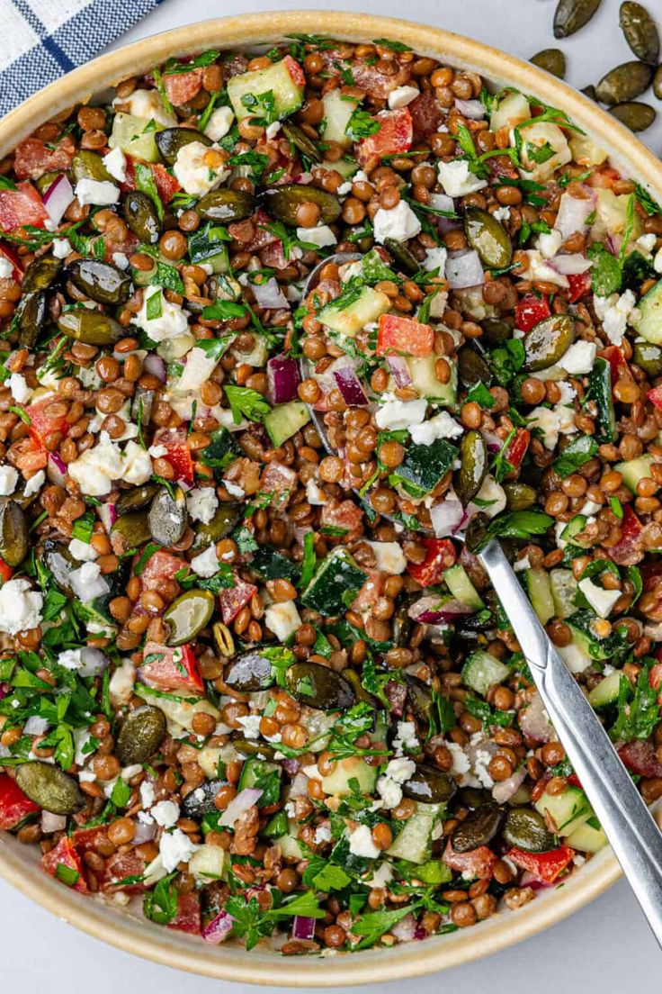 a bowl filled with lentils, vegetables and feta cheese next to a spoon