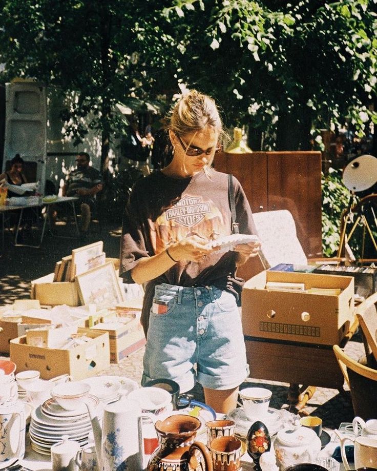 a woman standing in front of a table filled with dishes and cups, reading a book