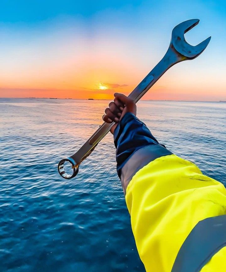 a person holding a wrench in their hand over the ocean at sunset or sunrise