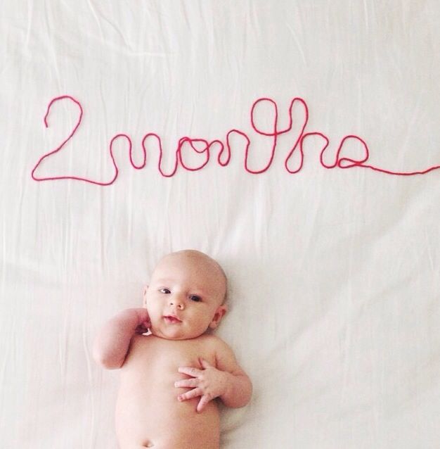 a baby laying on top of a bed next to the word 2 months written in red thread