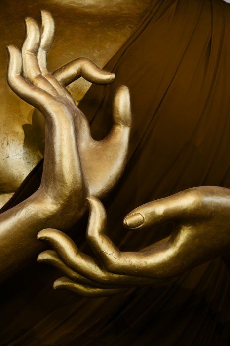 two hands touching each other in front of a gold statue that looks like they are hugging