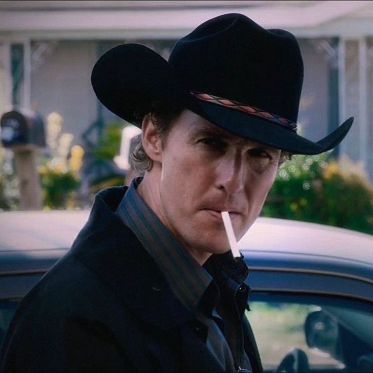 a man wearing a black cowboy hat standing in front of a car