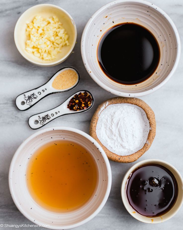 several different types of sauces and spoons on a white counter top with various ingredients