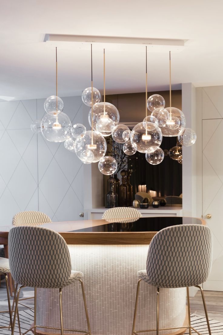 a modern kitchen with an island and marble counter tops, hanging lights over the dining room table