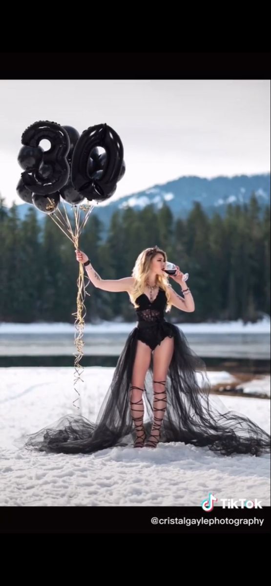 a woman holding two black balloons in the snow