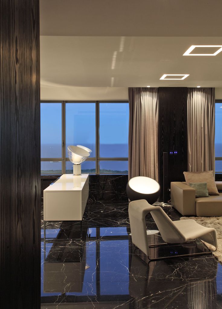 a living room with black marble floors and large windows looking out onto the ocean at night