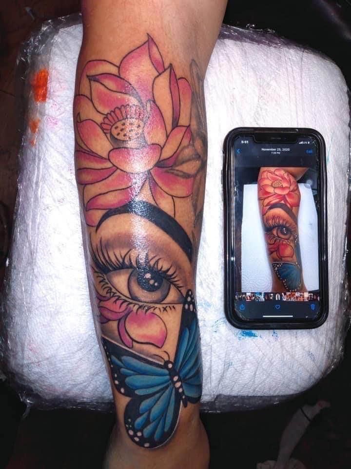 a woman's leg with an eye and flower tattoo on it, next to a cell phone