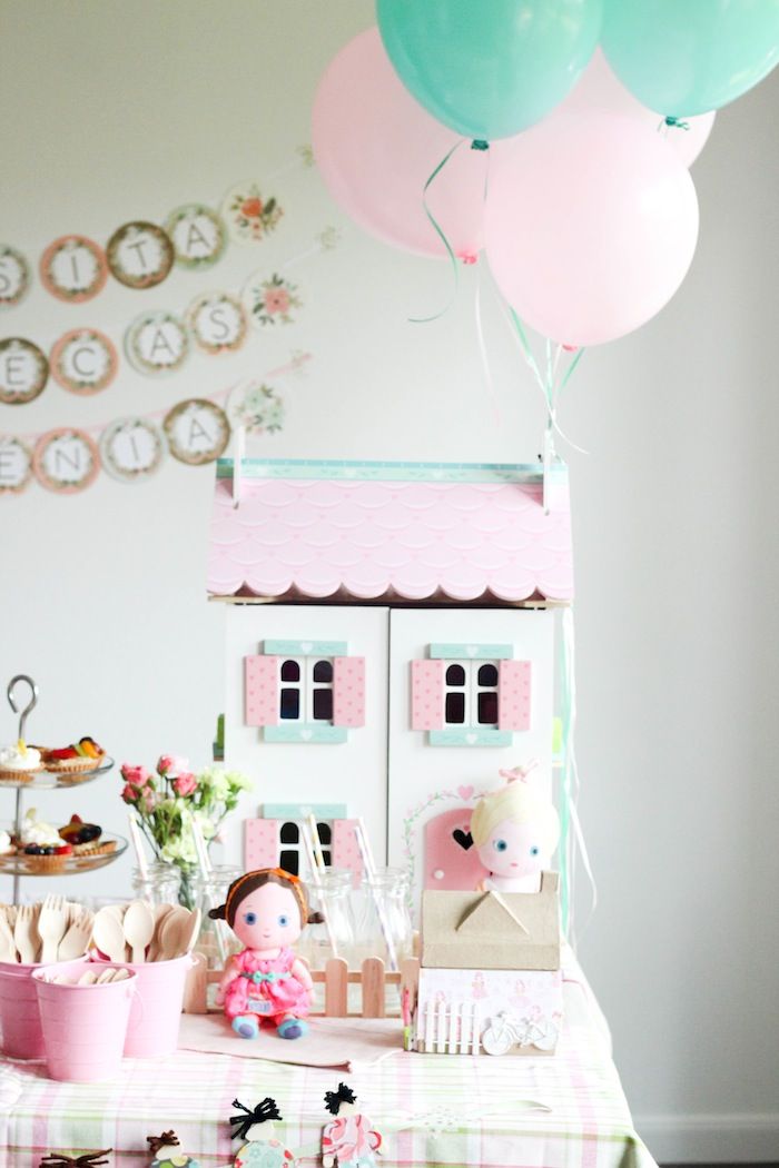 a table topped with lots of balloons next to a doll house and cupcakes