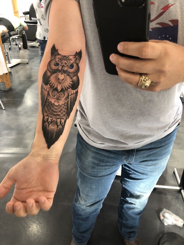 an owl tattoo is on the arm of a man who is holding a cell phone