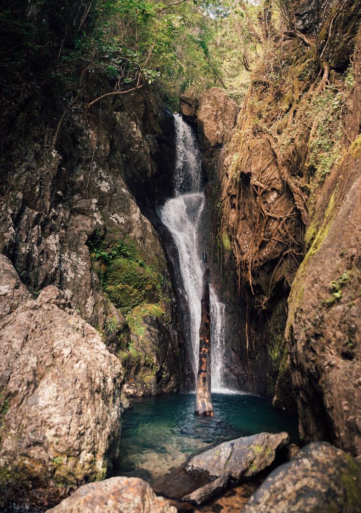 a man standing in the middle of a pool next to a waterfall