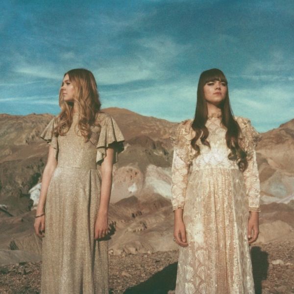 two women in long dresses standing on top of a mountain with mountains in the background