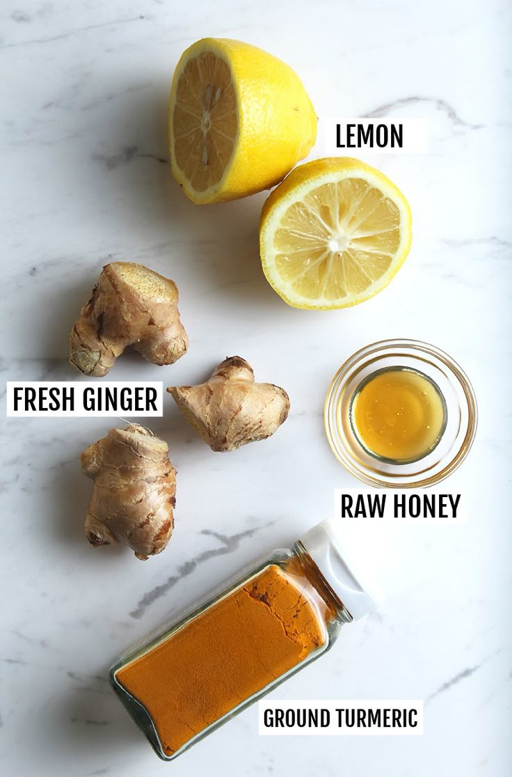 the ingredients to make ginger tea on a marble countertop with lemons, fresh ginger, and raw honey