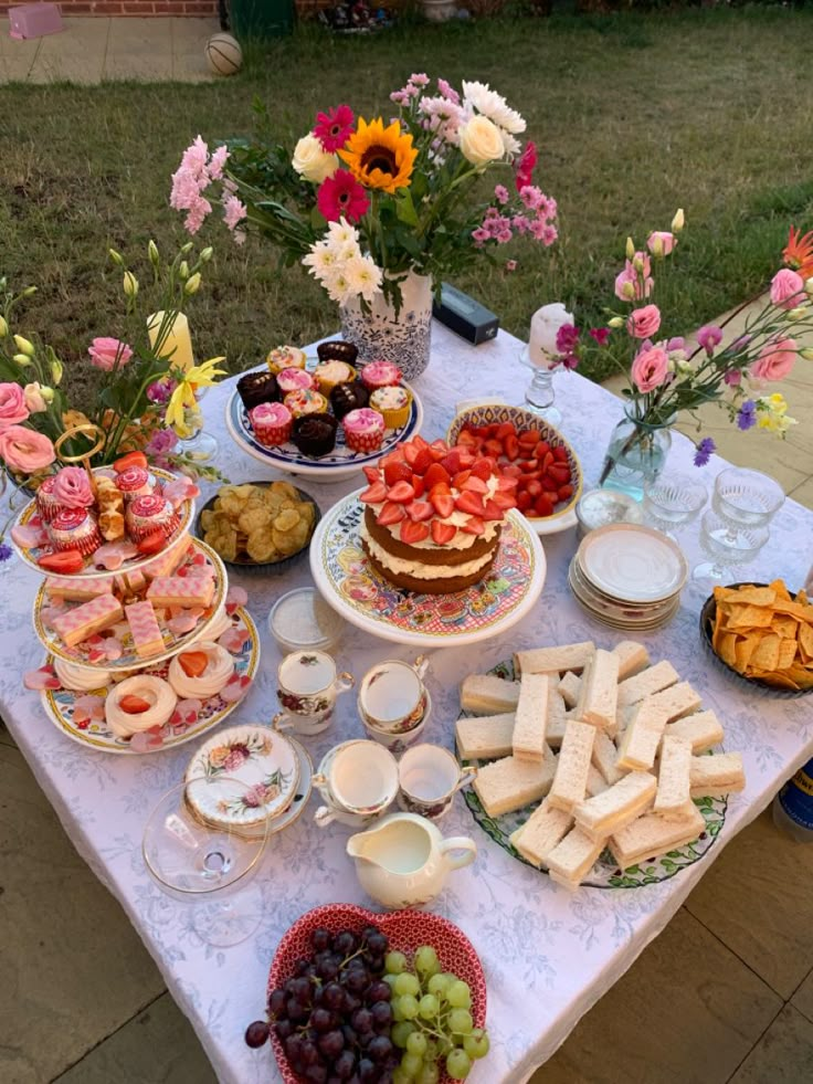 a table topped with lots of food on top of a lush green field next to flowers