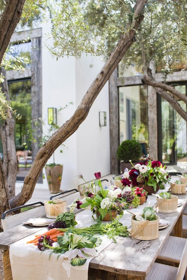 an outdoor table is set up with fresh flowers and greenery on it for a meal