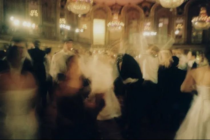 blurry photograph of people dancing at a wedding reception in an ornate room with chandeliers