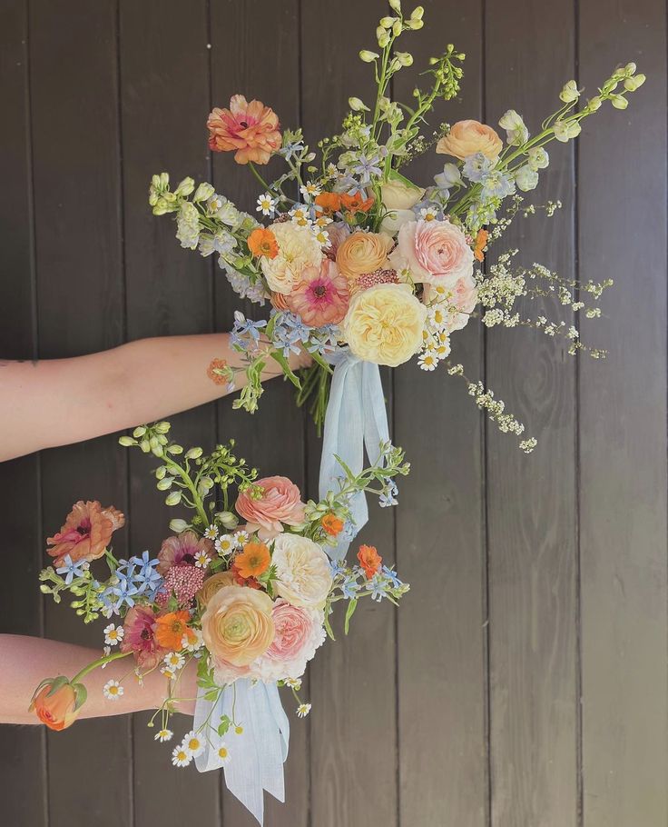 two bouquets of flowers are being held by someone's hand on a wooden background