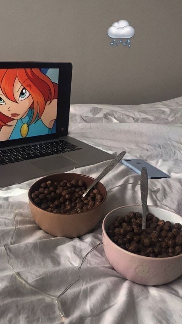 a laptop computer sitting on top of a bed next to two bowls filled with food