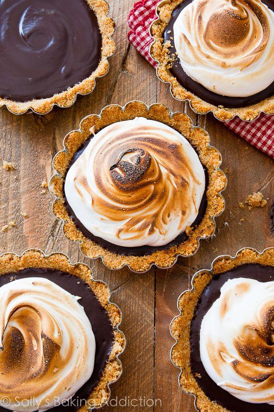 four pies with chocolate and white frosting on top sitting on a wooden table