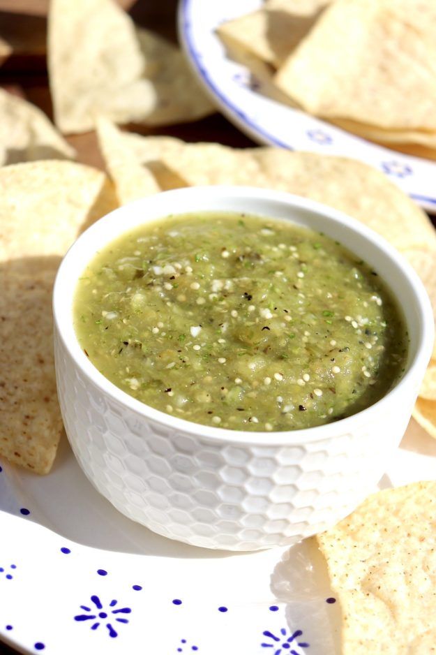 a white bowl filled with green salsa surrounded by tortilla chips