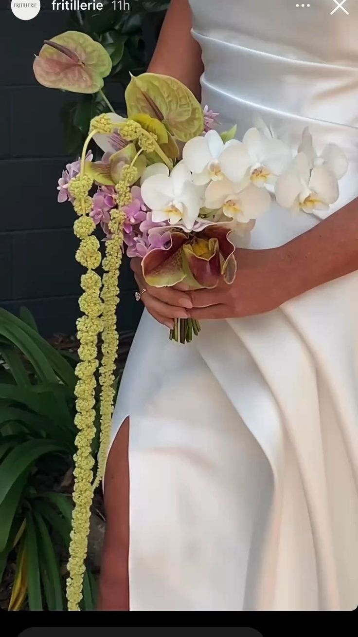 a woman in a white dress holding a bouquet of orchids and other greenery