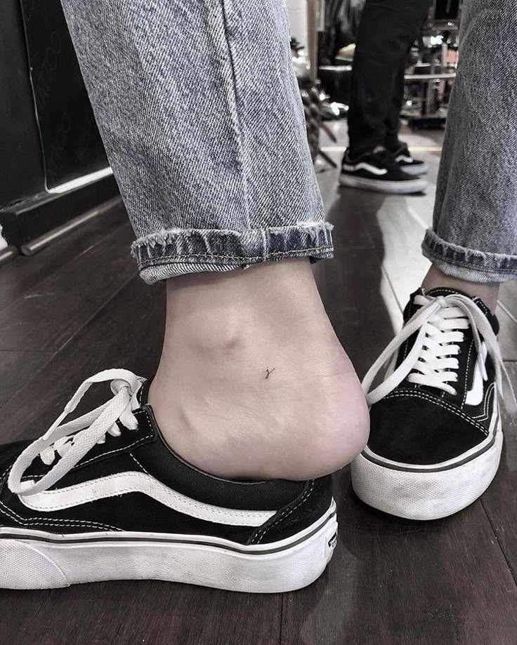 a person's foot with a small tattoo on their left ankle and black and white shoes