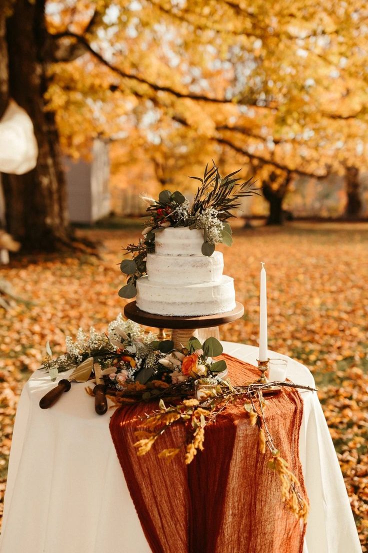 a wedding cake sitting on top of a table covered in leaves