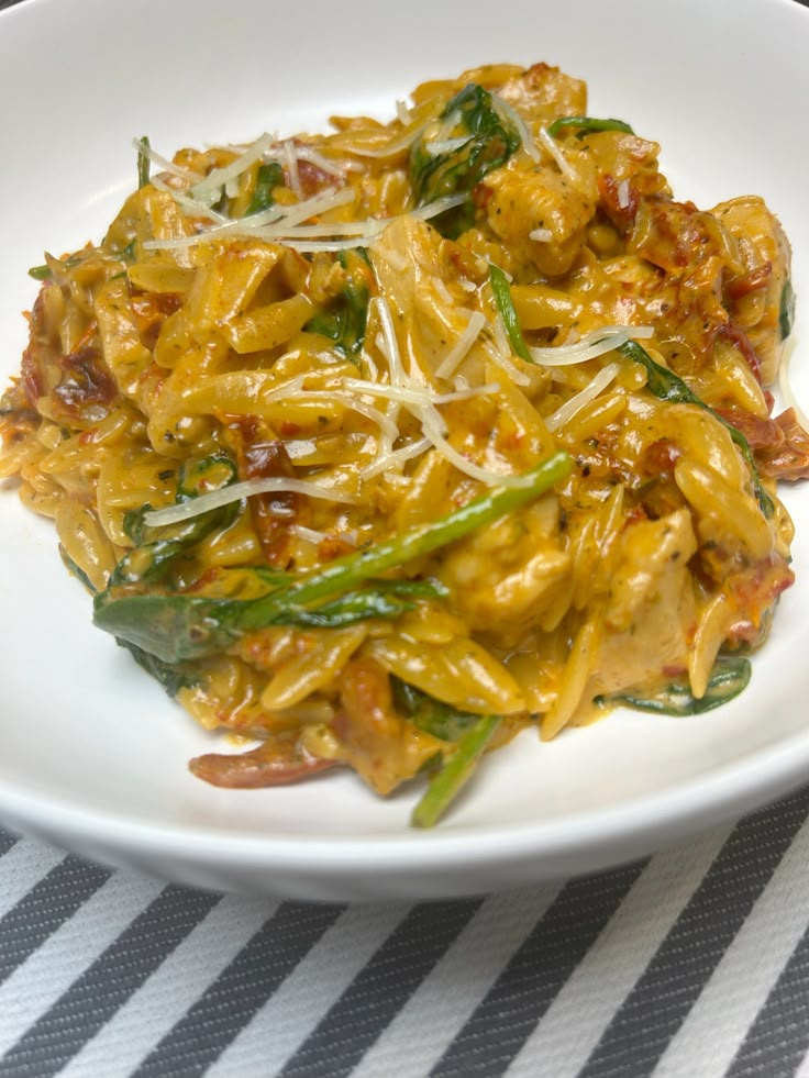 a white plate topped with pasta covered in cheese and vegtables on top of a striped table cloth