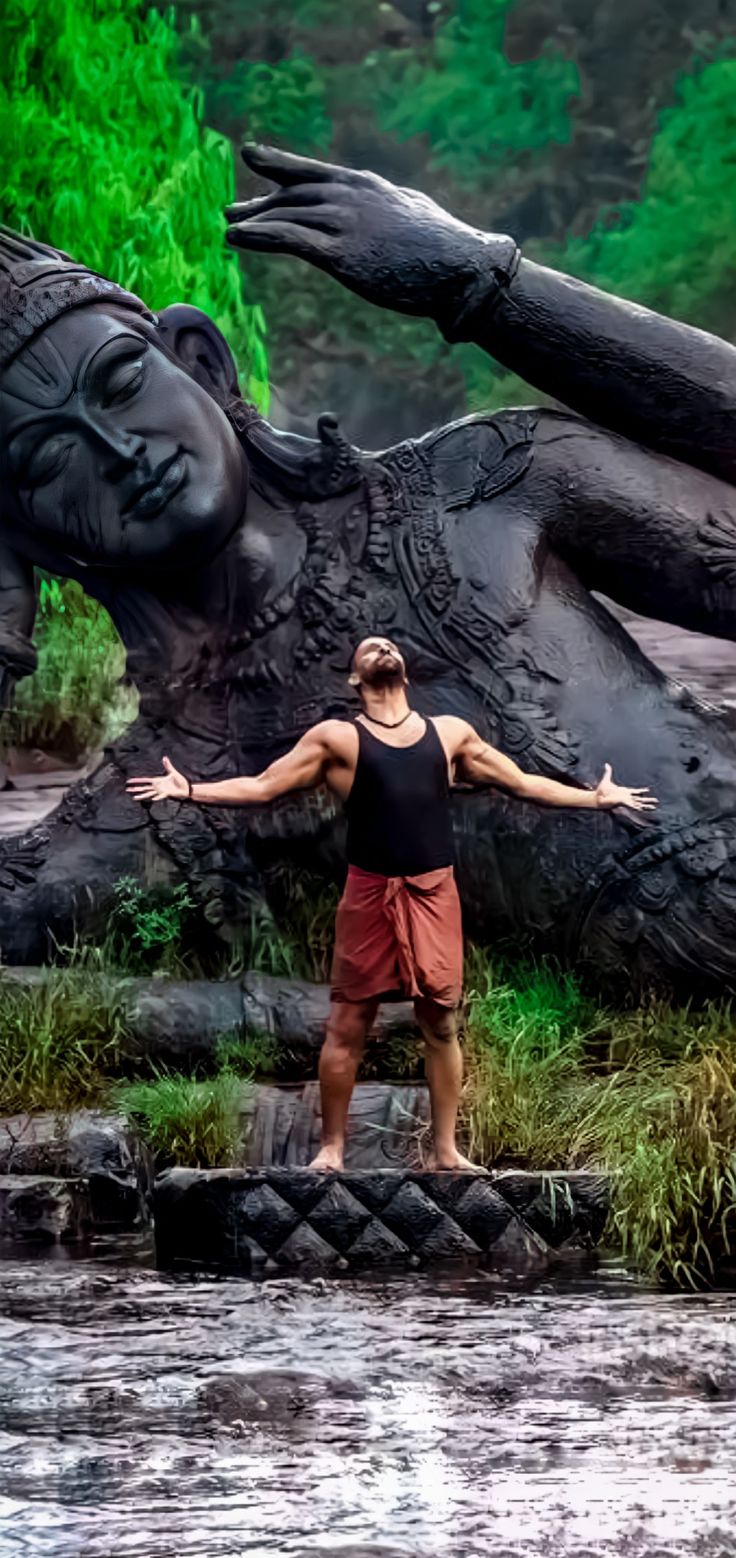 a man standing in the water with his arms spread out, next to a statue