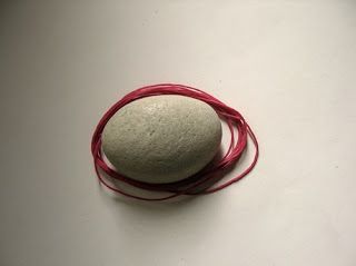 a round rock sitting on top of a white table next to a red string with a knot around it