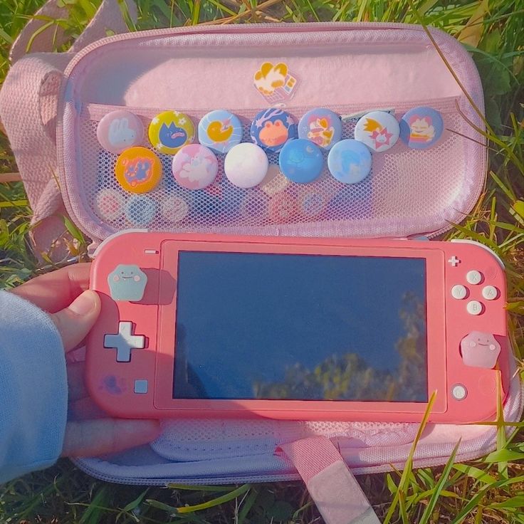 a pink nintendo wii game system sitting on top of the grass next to a person's hand