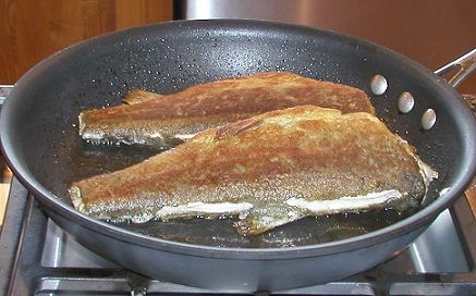 two fish cooking in a frying pan on the stove