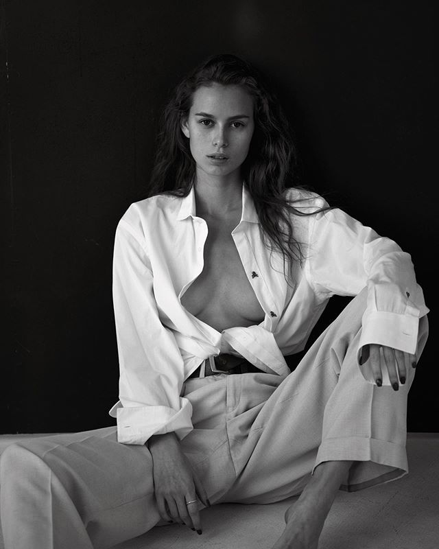 a black and white photo of a woman sitting on the ground with her shirt open