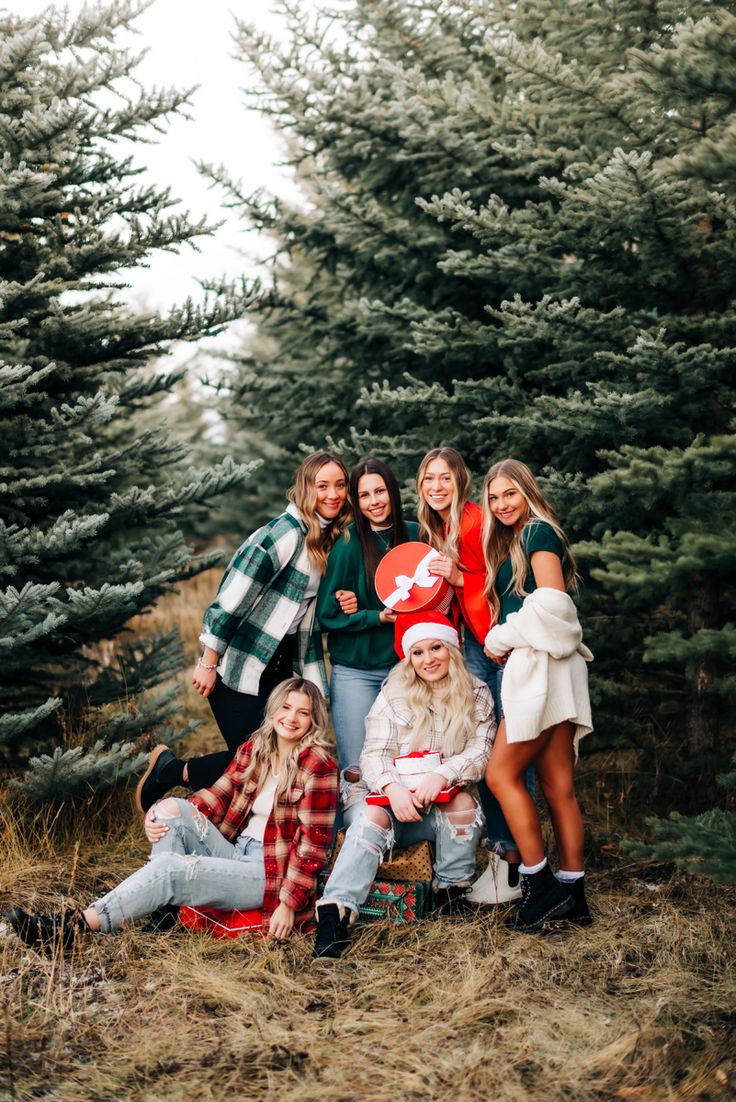 a group of young women standing next to each other in front of some pine trees