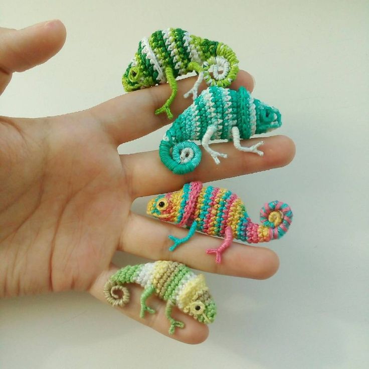 a person's hand holding three small crocheted animals in different colors and sizes