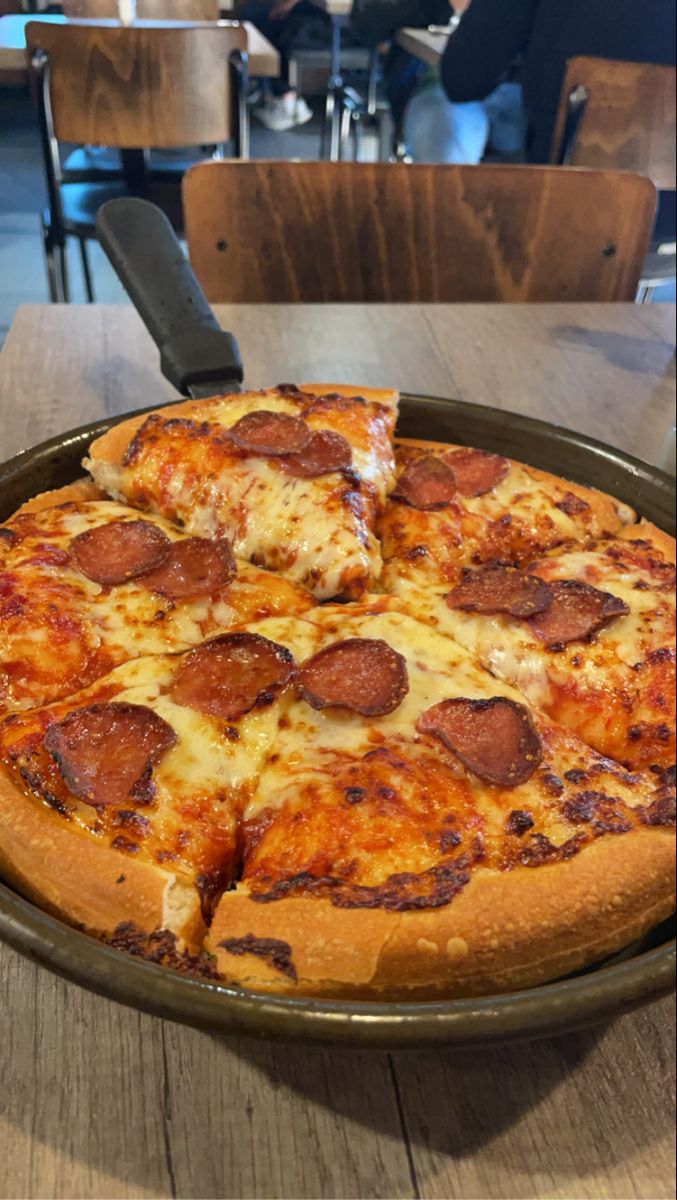 a pepperoni pizza sitting on top of a metal pan next to a wooden table