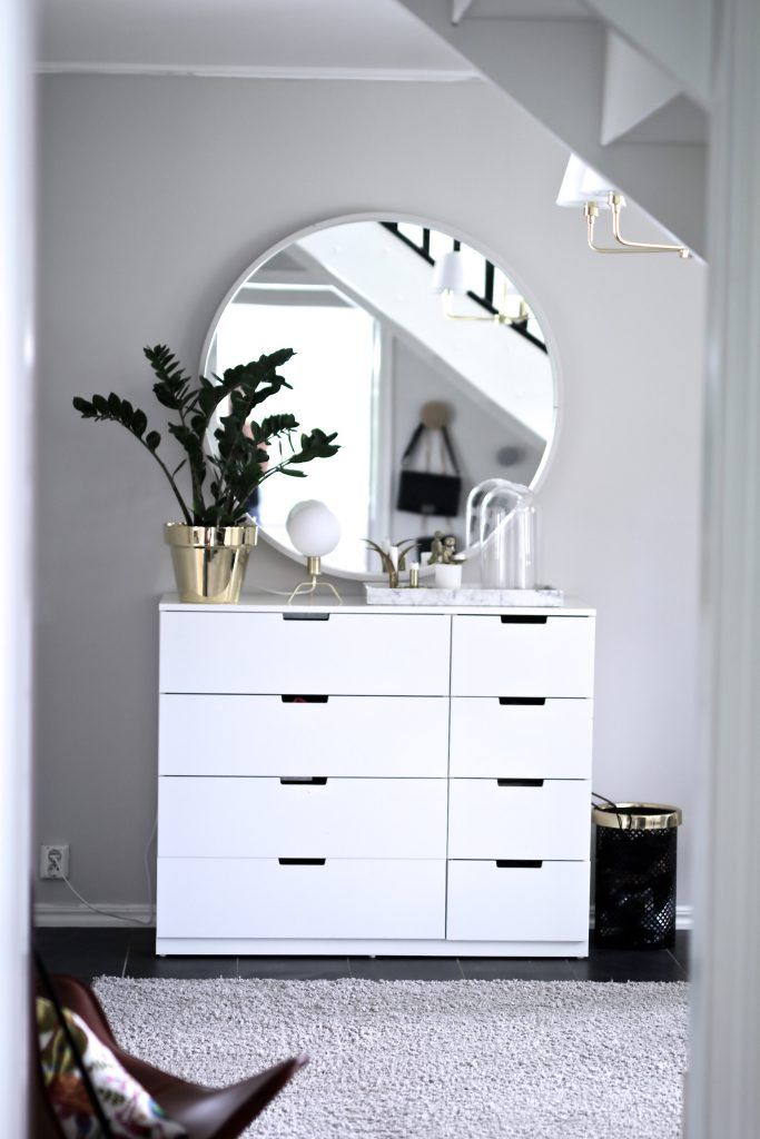 a white dresser sitting under a large mirror next to a chair and potted plant