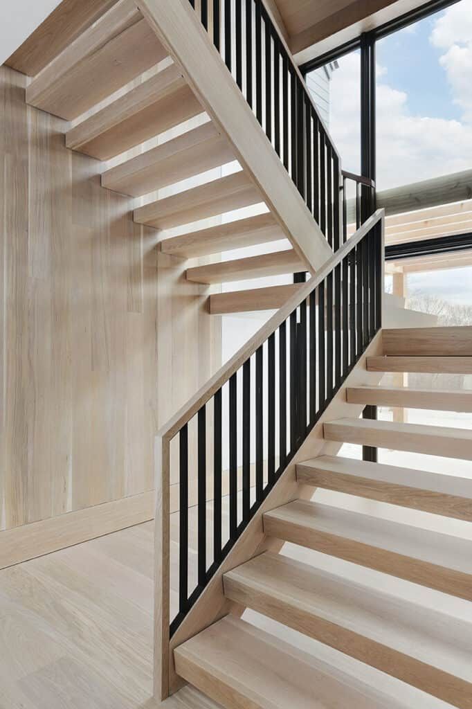 a wooden staircase with black handrails next to a window