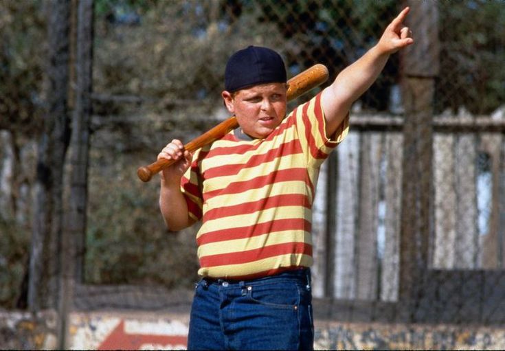 a young boy holding a baseball bat in his right hand and pointing to the side