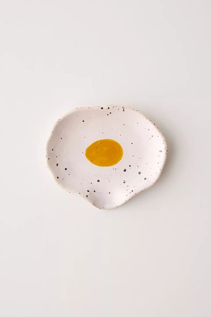 an egg shell shaped dish with black speckles sits on a white table top