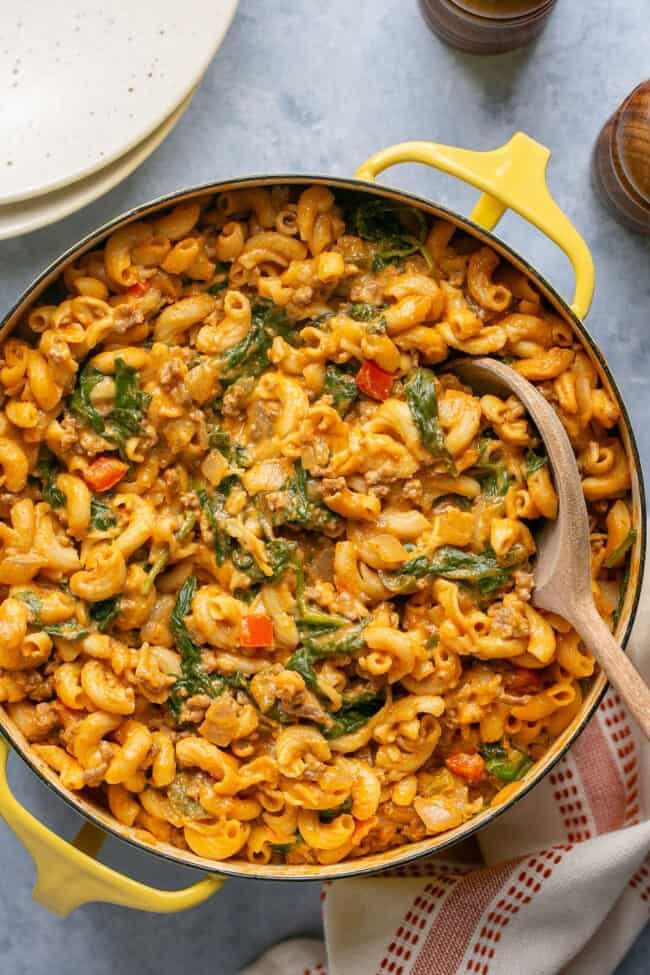 a yellow pot filled with pasta and spinach on top of a blue countertop