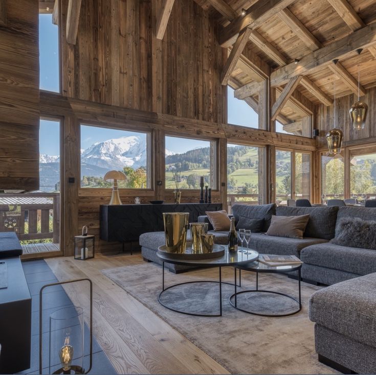 a living room filled with lots of furniture and large windows covered in wooden paneling