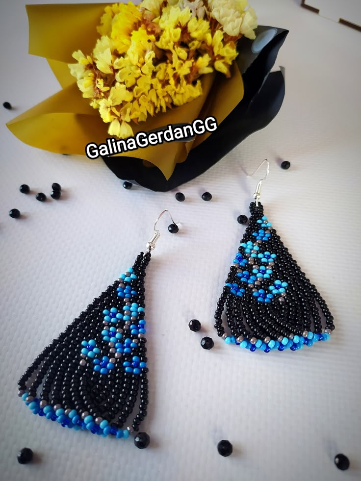 a pair of blue and black beaded earrings sitting next to a bouquet of flowers