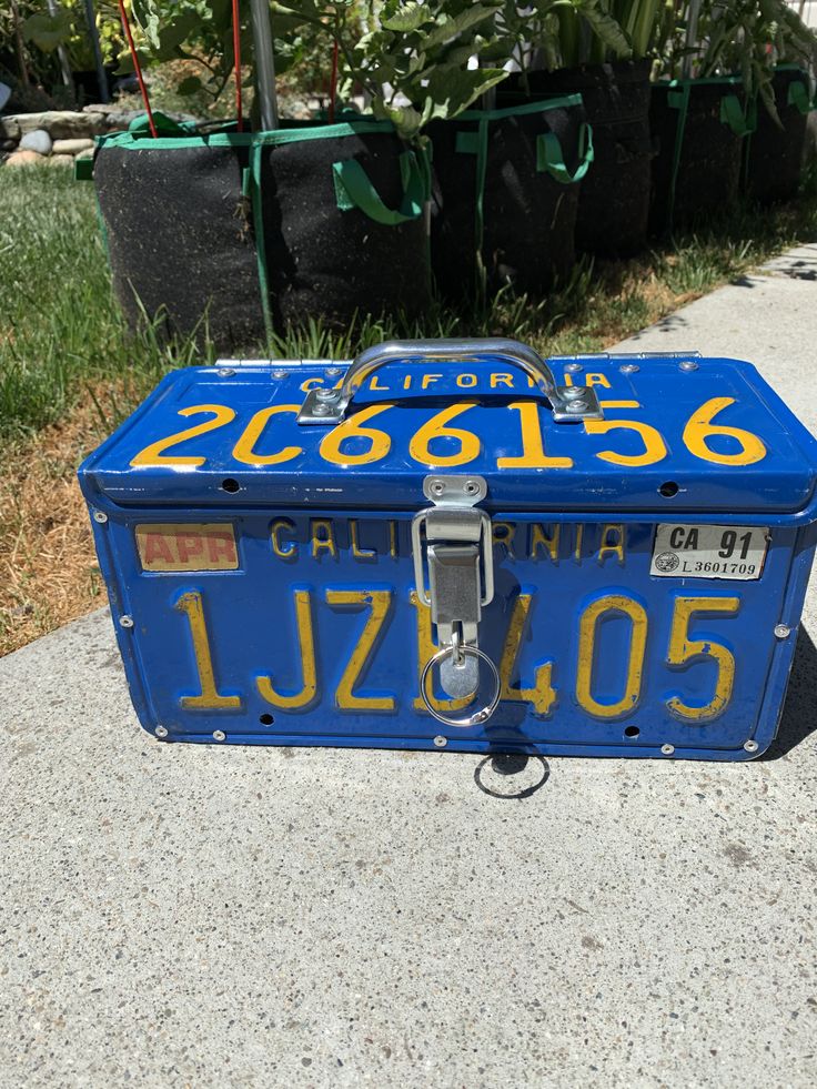 a blue box with yellow numbers on it sitting in front of some potted plants