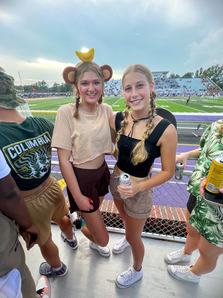 two girls standing next to each other at a sporting event with beer in their hands