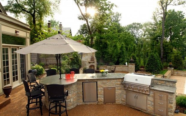 an outdoor kitchen with grill, table and chairs under an umbrella in the middle of it