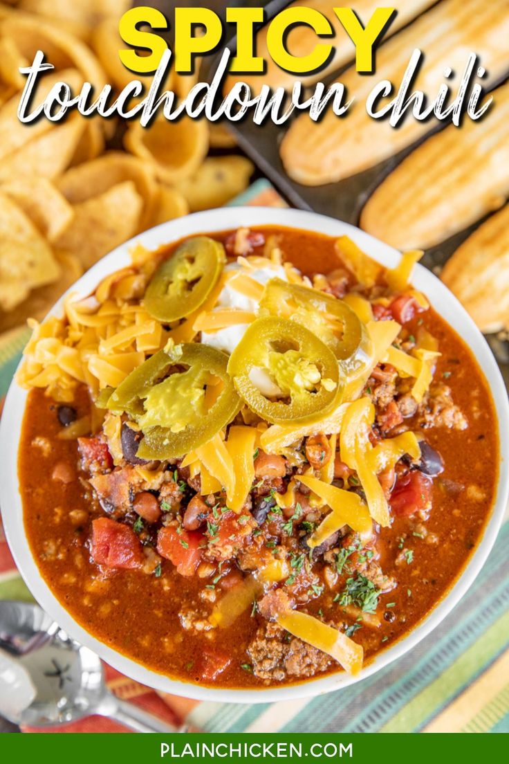 a white bowl filled with chili and cheese on top of a colorful table cloth next to crackers