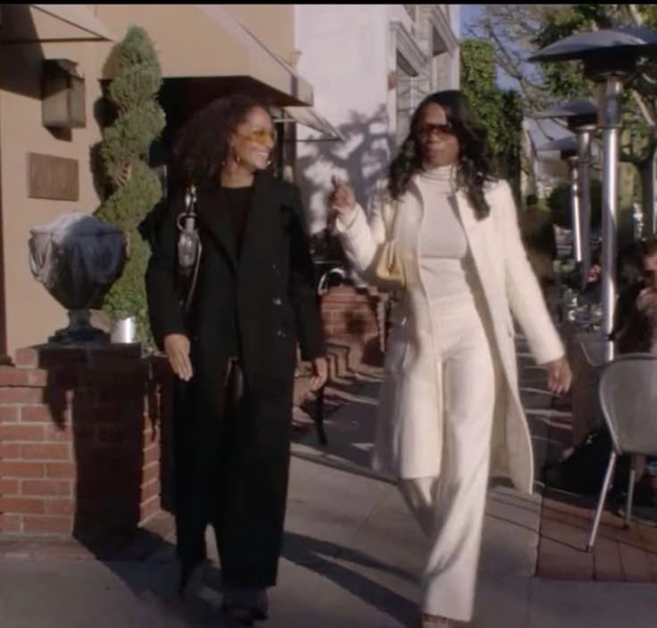 two women are walking down the street together, one is holding her hand and the other is wearing sunglasses