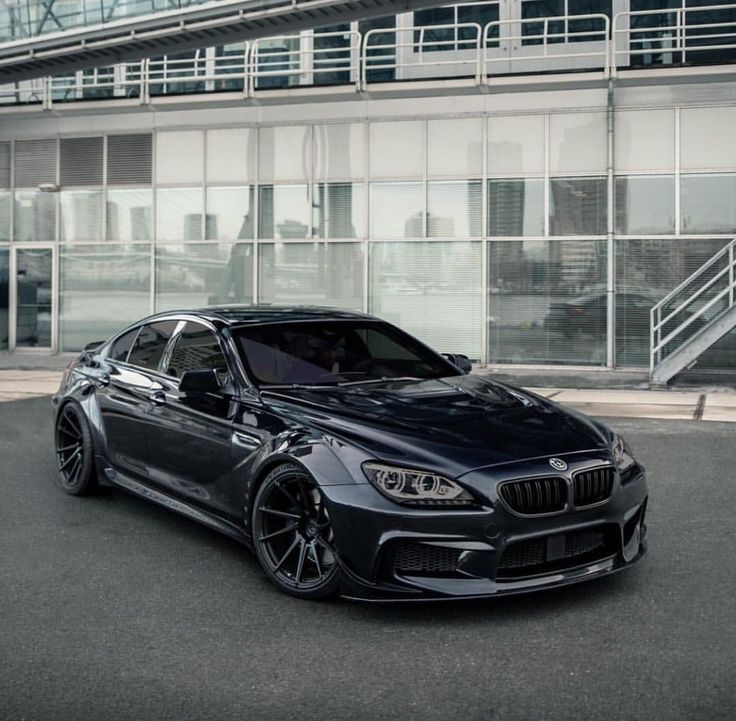 a black bmw is parked in front of a large glass building with stairs leading up to it