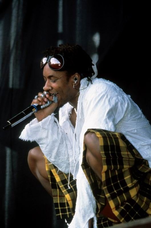 a man in white shirt and yellow plaid pants holding a microphone to his mouth while standing on stage